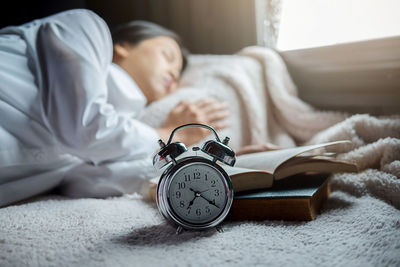 Woman sleeping by book and alarm clock on bed