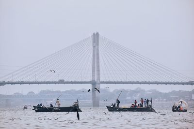 People on boat against sky and hanging bridge 
