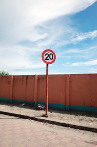 Speed limit sign on sidewalk against sky