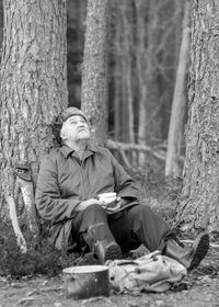 Black and white photo of a forester by the fire, man drinking tea, blurred forest background, wild