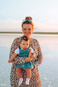 Happy smiling woman with red hair holding her child and walking by the sea