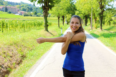 Portrait of smiling young woman exercising while standing on road