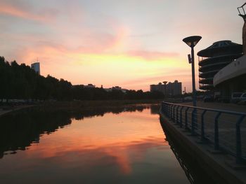 Scenic view of river by buildings against sky during sunset