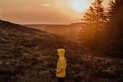 Person standing on land against sky during sunset