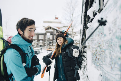 Man standing by confident woman pointing at map with ski pole