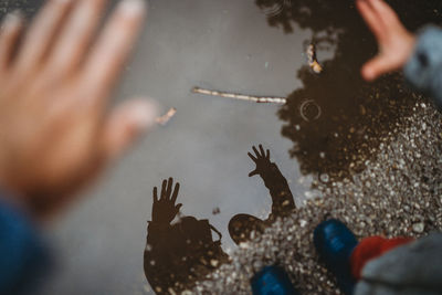 View from above reflection of hands on a puddle of mother and child