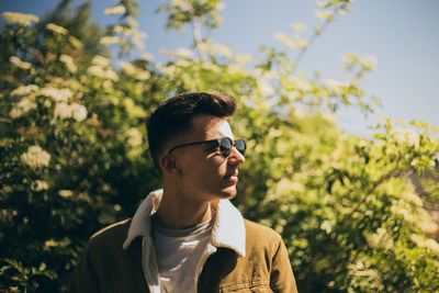 Portrait of young man looking away against trees