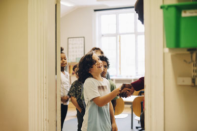 Teacher shaking hand with schoolboy in row at doorway