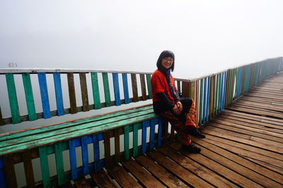 Portrait of woman sitting by railing against sky