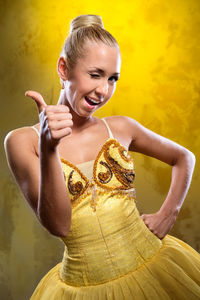 Portrait of beautiful ballerina showing thumbs up against yellow background