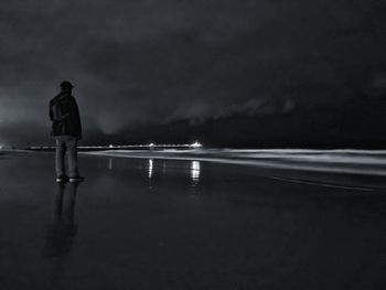 Rear view of man standing at beach against sky at night