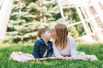 Family, mom and her son lie on the grass in the park in summer and kiss