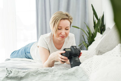 Young man photographing while sitting on bed