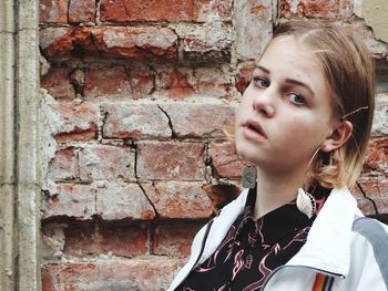 Portrait of woman looking away against brick wall