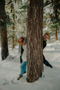 Portrait of couple standing by tree trunk during winter