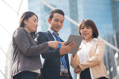 Business people using digital tablet while standing on city street