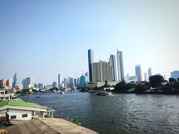 Modern buildings by river against clear sky