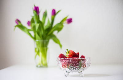 Strawberries in bowl by flower vase on table at home