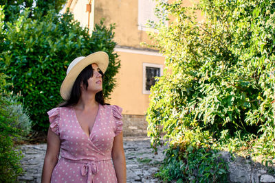 Portrait of a beautiful young woman in pink dress, hat, green, plants.