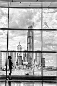 Woman standing by glass window against buildings in city