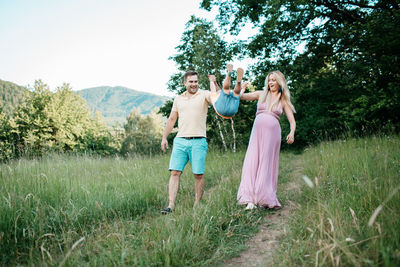 Parents swinging baby boy while walking on field