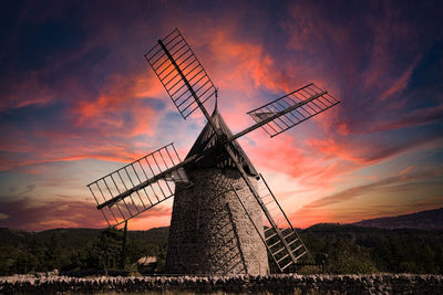 Low angle view of traditional windmill on field against sky during sunset
