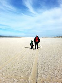 Man with child and dog walking on landscape against sky