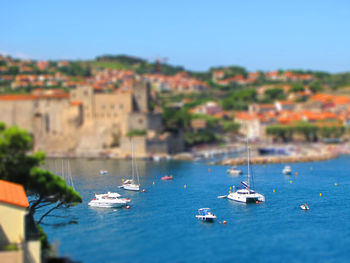 Boats sailing in sea by townscape against sky