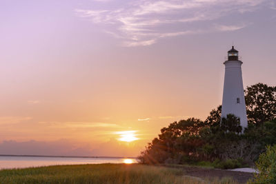 Lighthouse by sea against sky during sunset