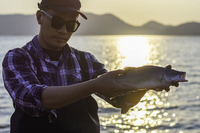 Man wearing sunglasses standing at beach against sky