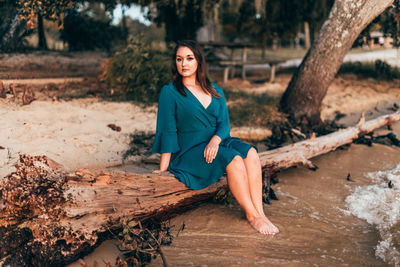 Full length portrait of young woman sitting on wood at beach