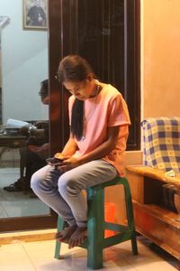 Full length of young man sitting on chair at home