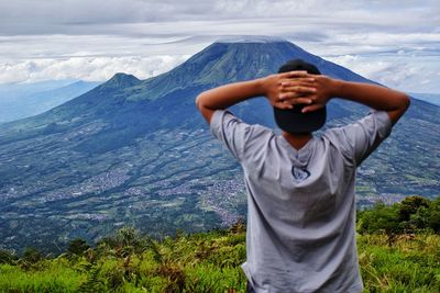 Rear view of man standing on mountain against sky