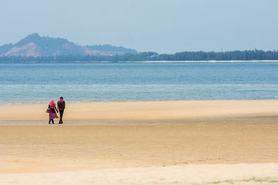 Couple walking at beach against clear sky