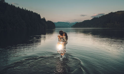 A woman holds young girl in lake against sthe ky during sunset