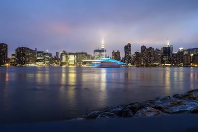 Illuminated buildings by river in city at night