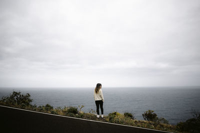 Back view of female traveler standing near asphalt road near sea on cloudy day in la palma, spain