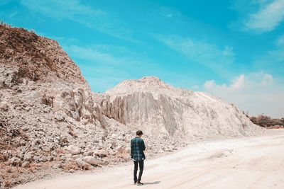 Rear view of man standing on rock against sky