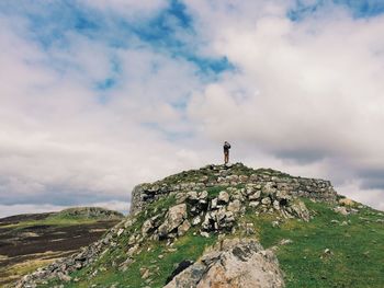 Low angle view of man standing on rock against cloudy sky