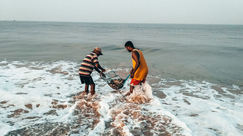 People on shore at beach against sky