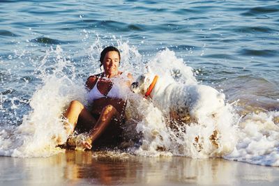 Woman with dog sitting at beach with splashing water in sea