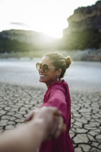 Smiling woman holding her hand for her boyfriend looking at the camera