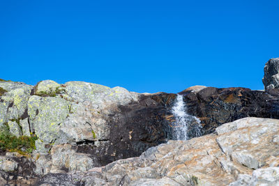 Low angle view of rocks against clear blue sky