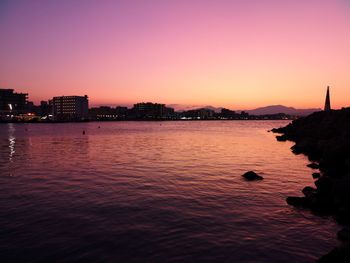 Silhouette city by sea against sky during sunset