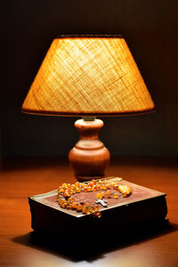 Soft light of table lamp. on table old prayer book and amber catholic rosary. religion. close-up.