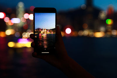 Cropped hand of woman using mobile phone at night