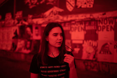 Beautiful young woman looking away while standing against wall