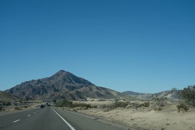 Road leading towards mountains against clear blue sky