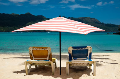 Deck chairs on beach against sky