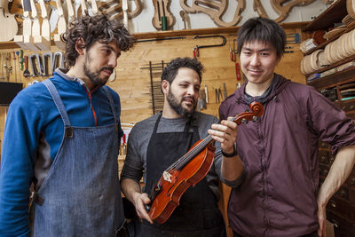 Two craftsmen violinmakers checking data and measures for a new violin with computer